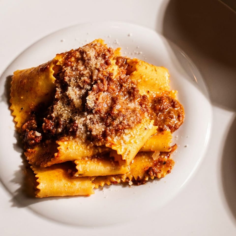 Pasta dish with ragu and grated cheese on a white plate, with other plates nearby.