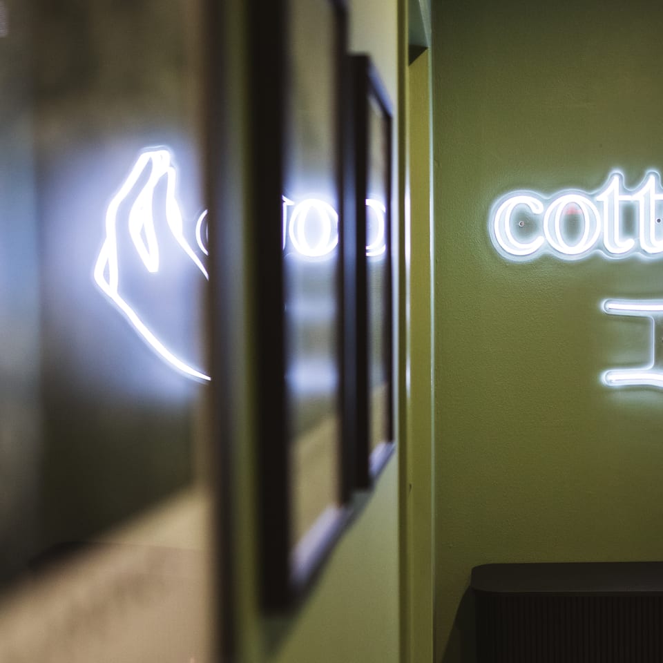 Glowing rabbit neon sign reading “cotton” on a green restaurant wall, reflected in a nearby mirror.