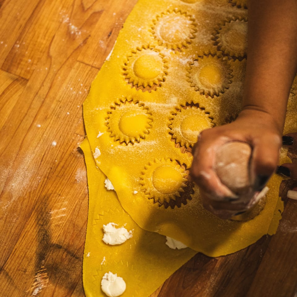 Fresh ravioli with fluted edges and creamy filling being prepared on a flour-dusted wooden worktable.