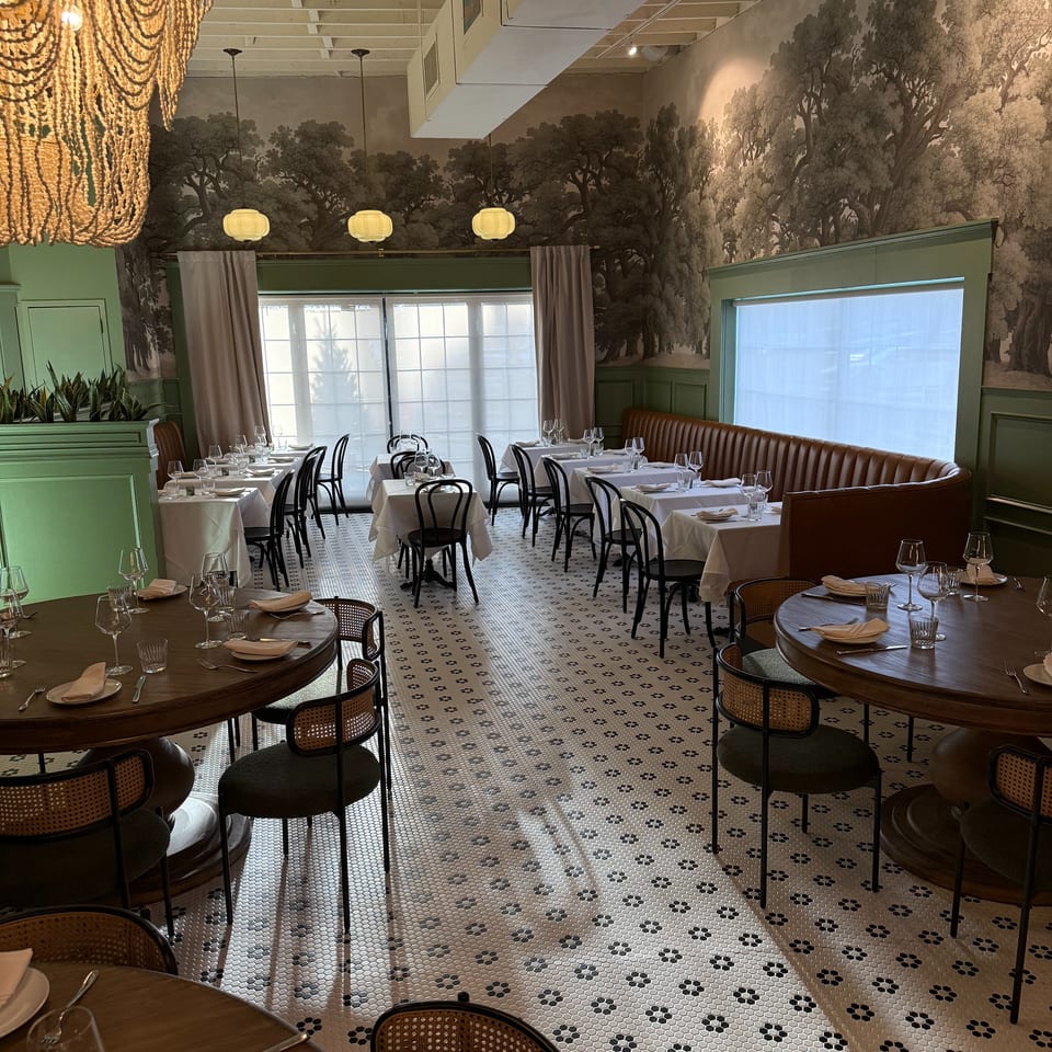 Elegant restaurant dining room with forest mural wallpaper, set tables, pendant lights, green walls, and patterned tile flooring.