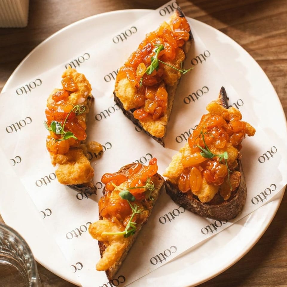 Four pieces of bruschetta topped with orange relish and microgreens on a white plate.